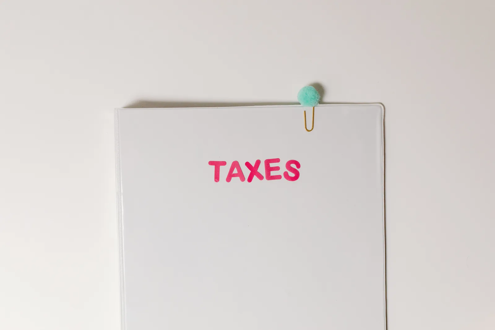 Close-up of a tax file with a pink 'TAXES' label and a paperclip, offering copy space and a conceptual minimalist design. How federal business tax costs add up over a year