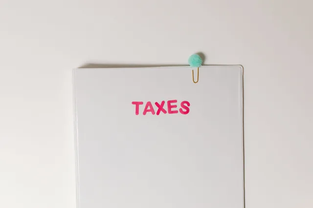 Close-up of a tax file with a pink 'TAXES' label and a paperclip, offering copy space and a conceptual minimalist design. How federal business tax costs add up over a year