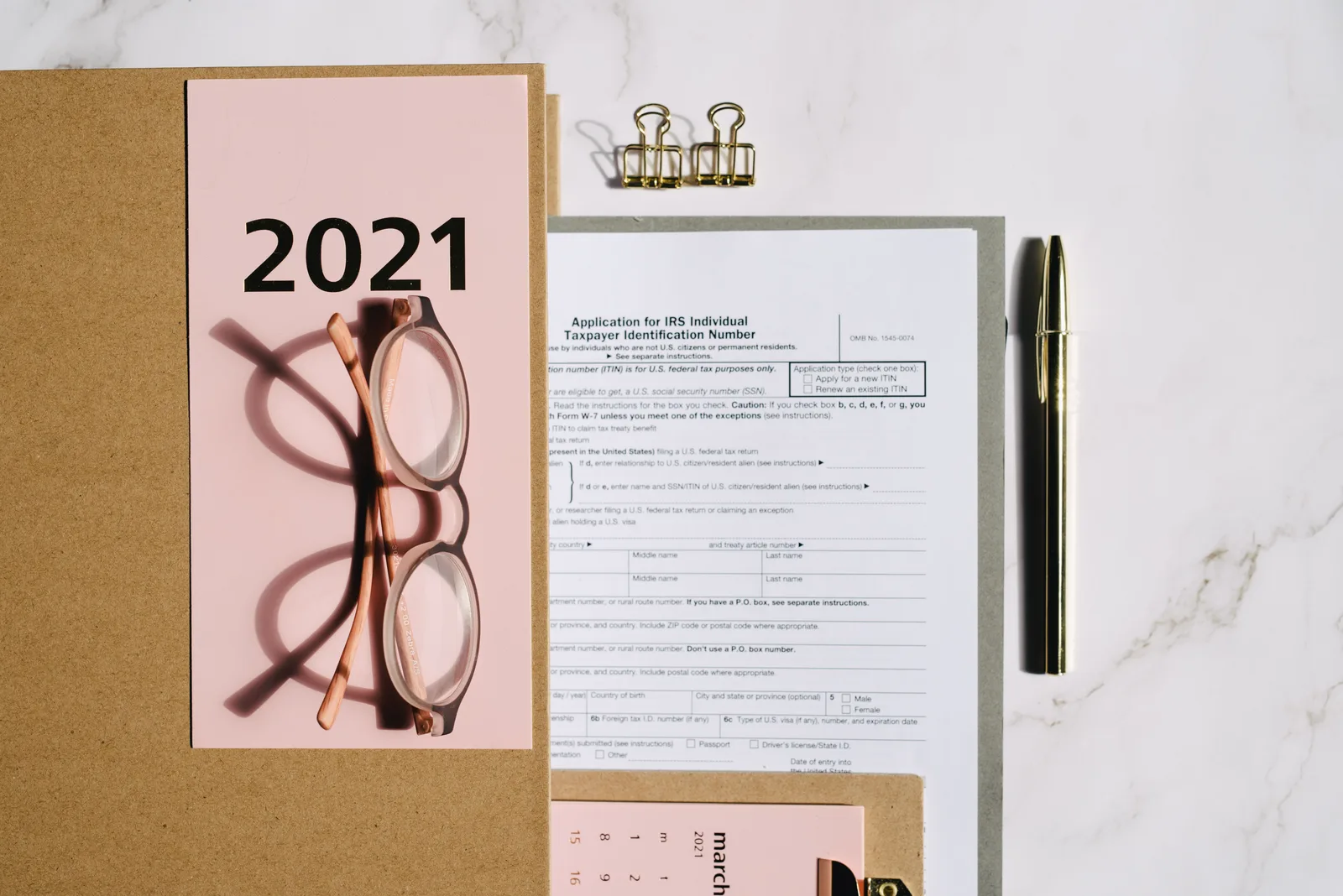 Flat lay image featuring 2021 tax documents, eyeglasses, and office supplies on a marble surface. Federal business tax examples: what decided each one